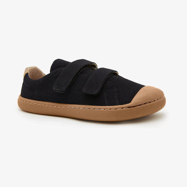 Black cotton canvas Kid's Hook & Loop sneaker by Origo with two straps and amber gum sole, angled side view.